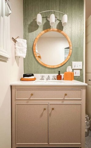 A bathroom with a round mirror, a towel rack, a sink with toiletries, and a cabinet. - Chic King Suite | Downtown Ashland | Pet Friendly (Ashland)
