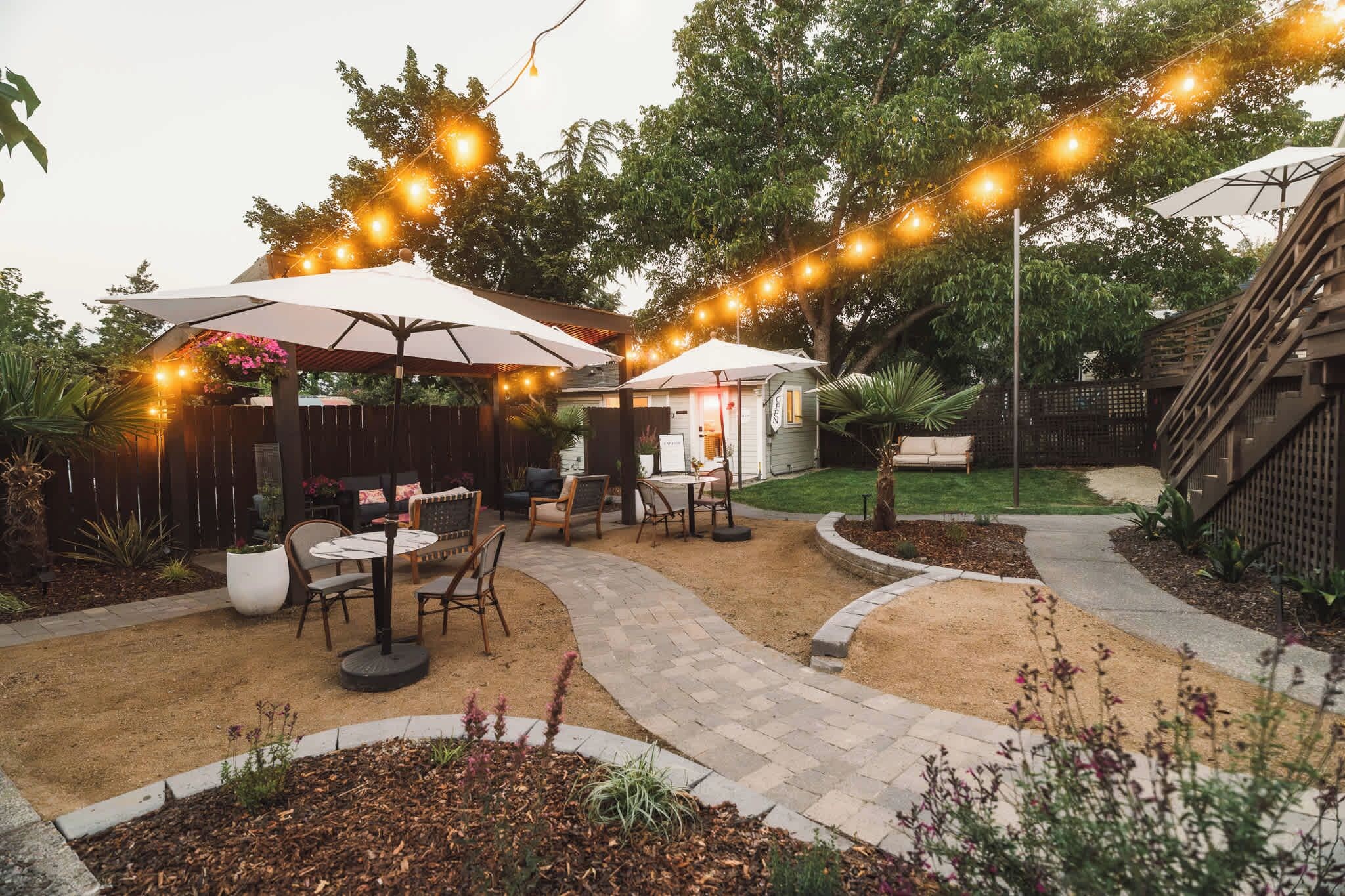 An outdoor patio area with string lights, a covered seating area, and a pathway.