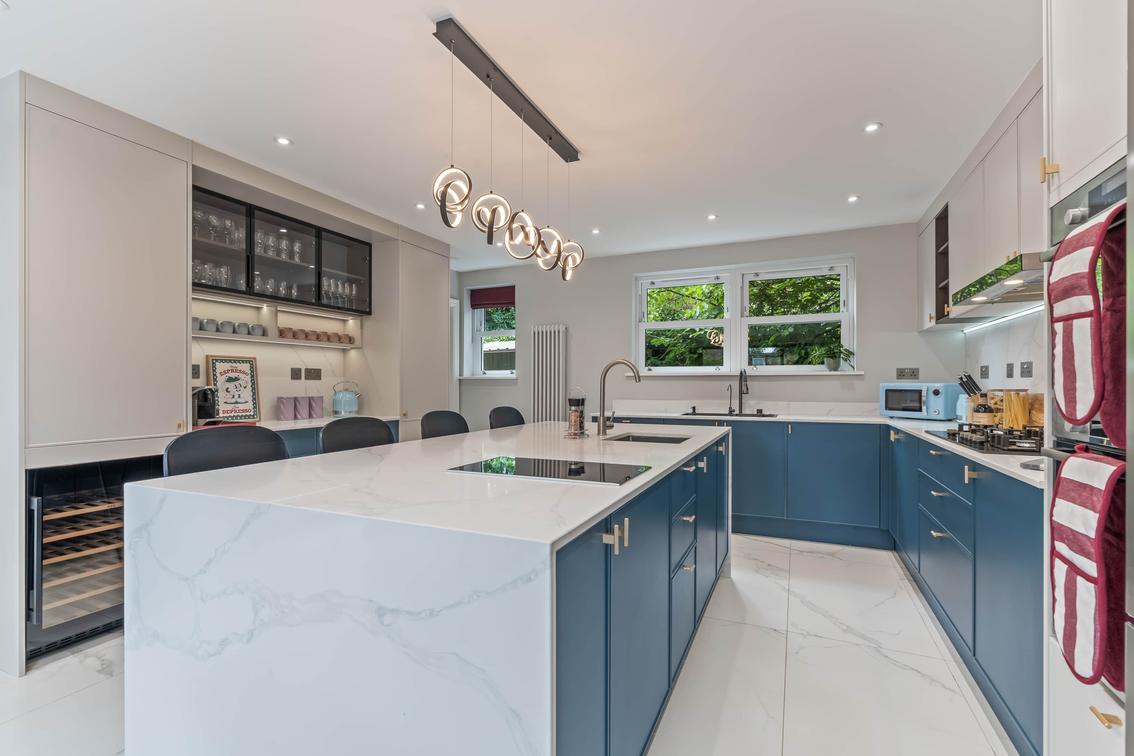 A modern kitchen with a marble island, blue cabinets, and a unique circular light fixture.