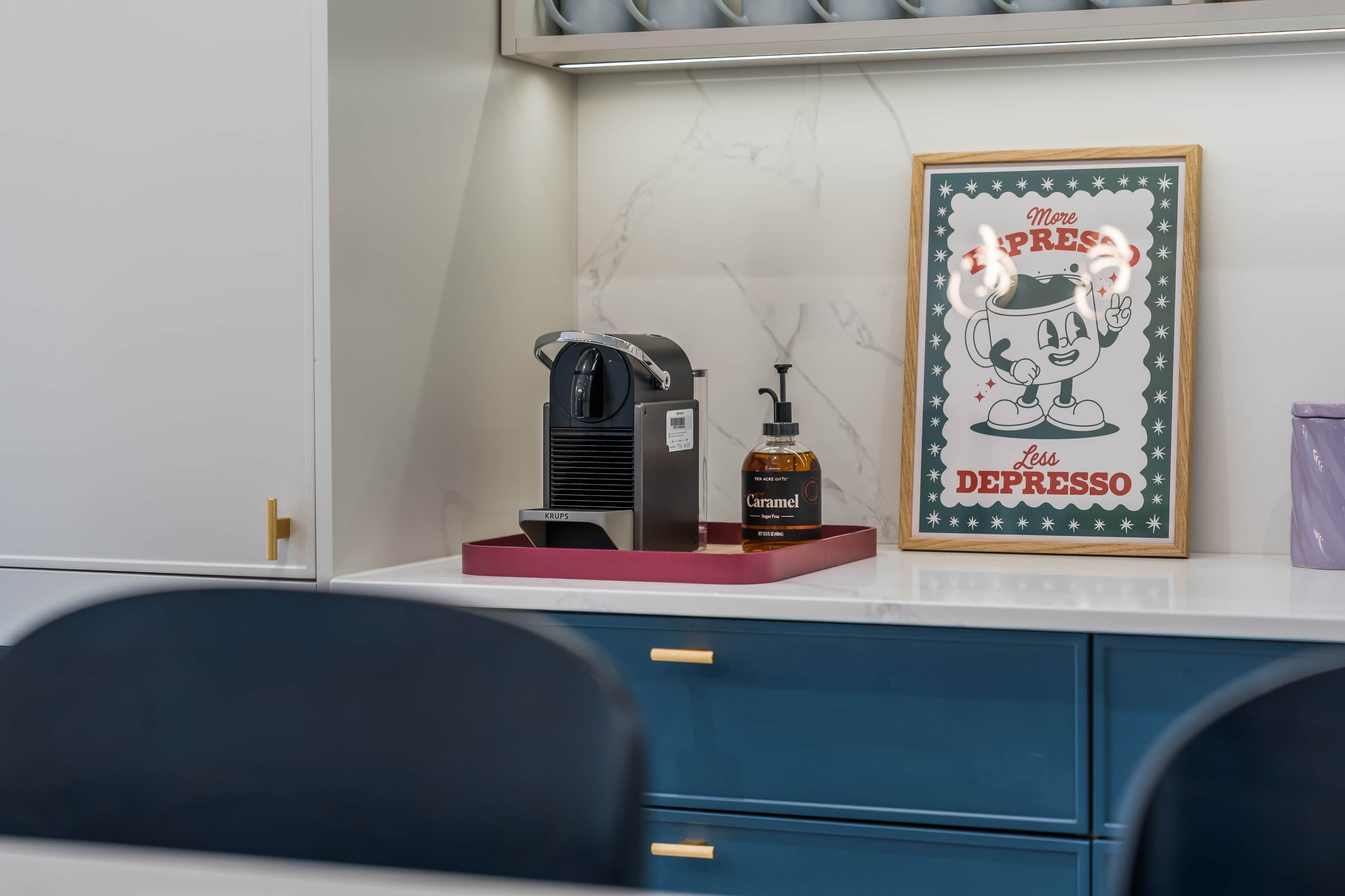 A coffee machine, a sugar-free caramel syrup bottle, and a framed motivational quote on a counter.