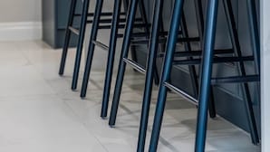 Une cuisine dotée d’un coin bar comprenant quatre tabourets de bar noirs à pieds métalliques et un robinet moderne.