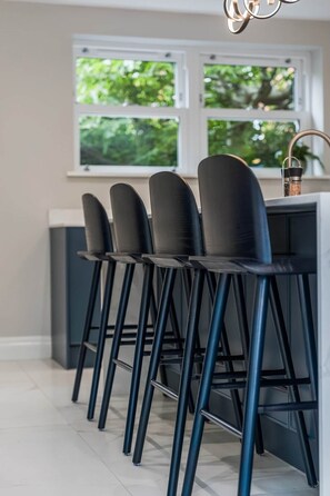 Una cocina con barra equipada con cuatro taburetes negros de patas metálicas y un grifo moderno.