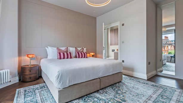 Une chambre à coucher moderne avec un grand lit, des lampes de chevet, un tapis à motifs et une vue sur l’extérieur.