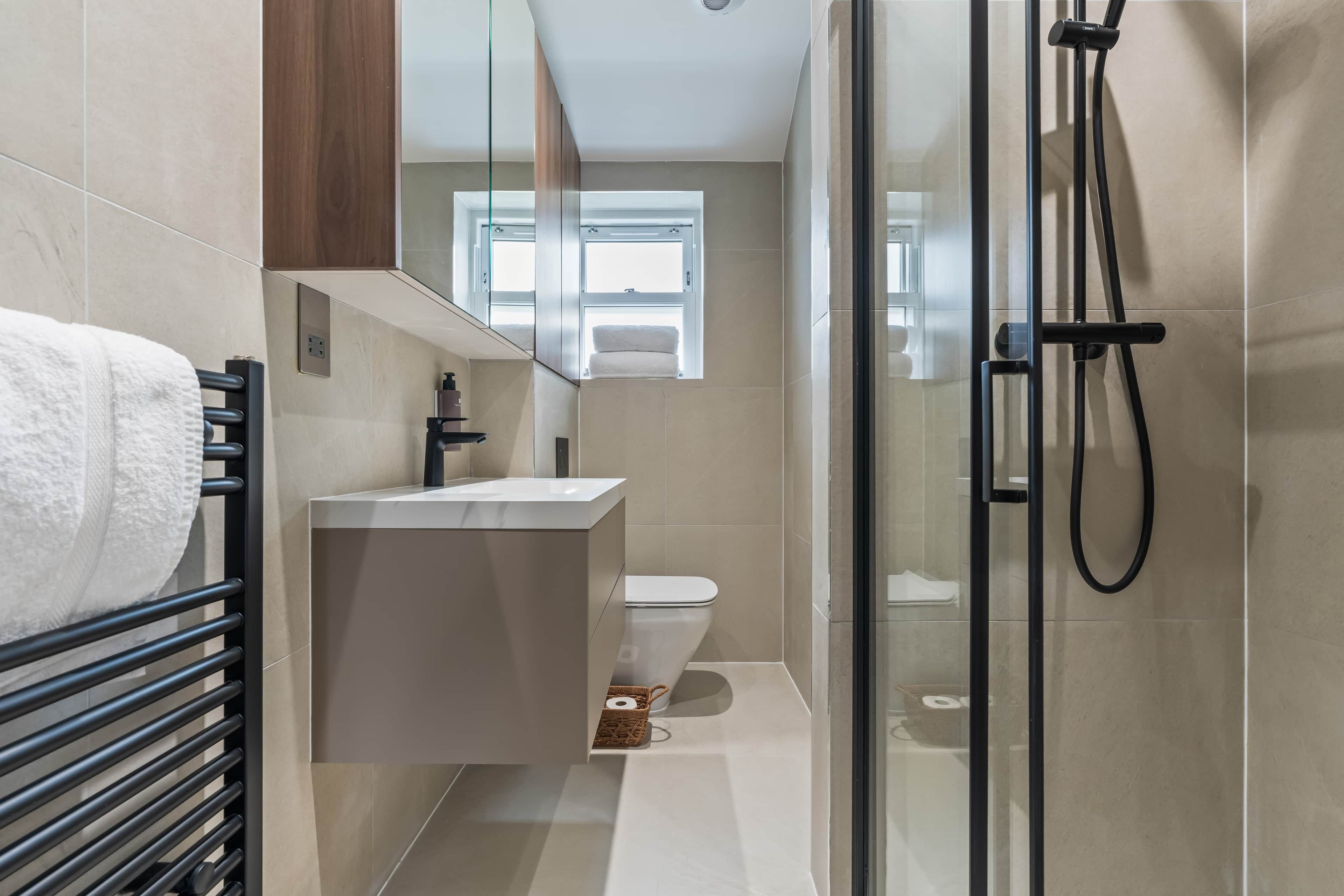 Een moderne badkamer met een glazen douchecabine, een witte wastafel en een toilet.