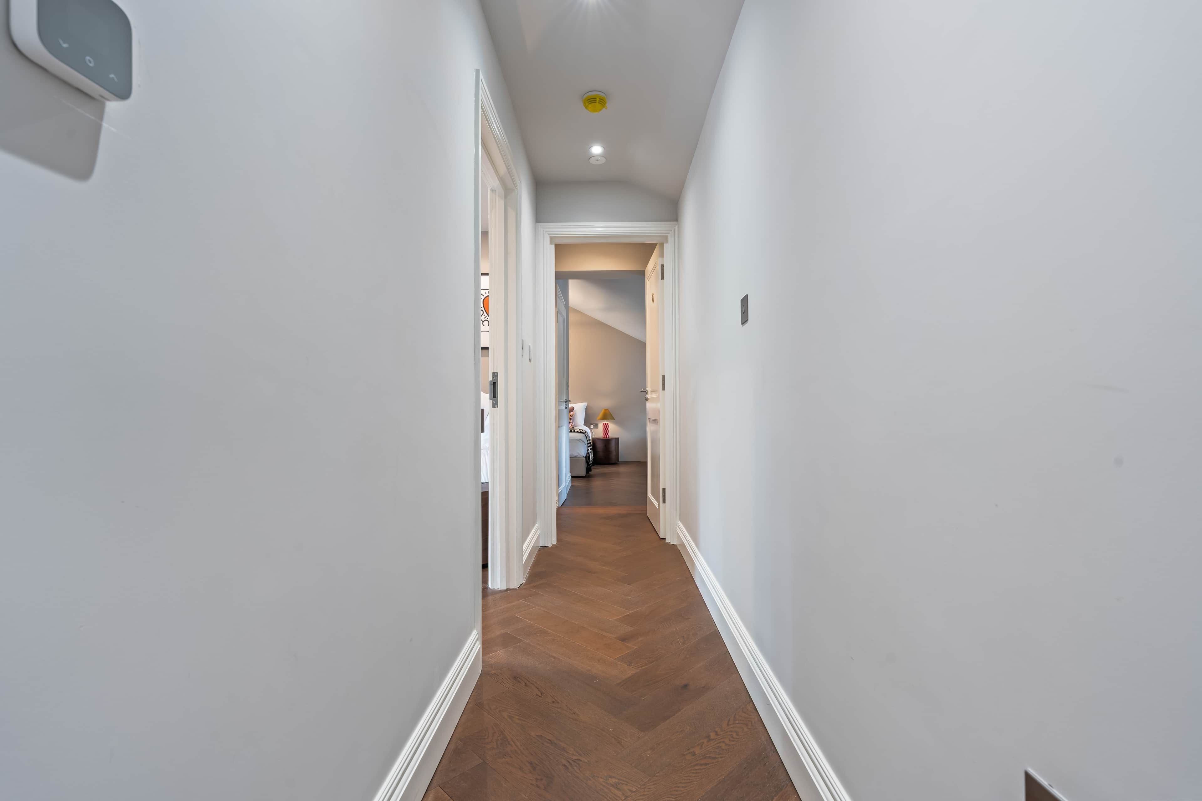 A hallway with a wooden floor, white walls, and a door leading to a bedroom.