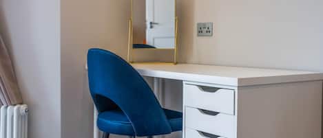 A room with a white desk, a blue chair, a mirror, and a radiator.