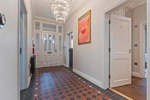 A hallway with a patterned floor, a chandelier, a door with a number, and a poster on the wall.