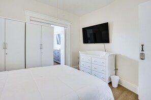 Une chambre à coucher comprenant un lit, une commode, un téléviseur et une porte donnant sur une autre pièce.