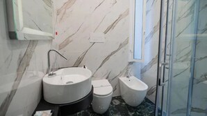 Un bagno con una parete in marmo, un lavandino, un water e un bidet.