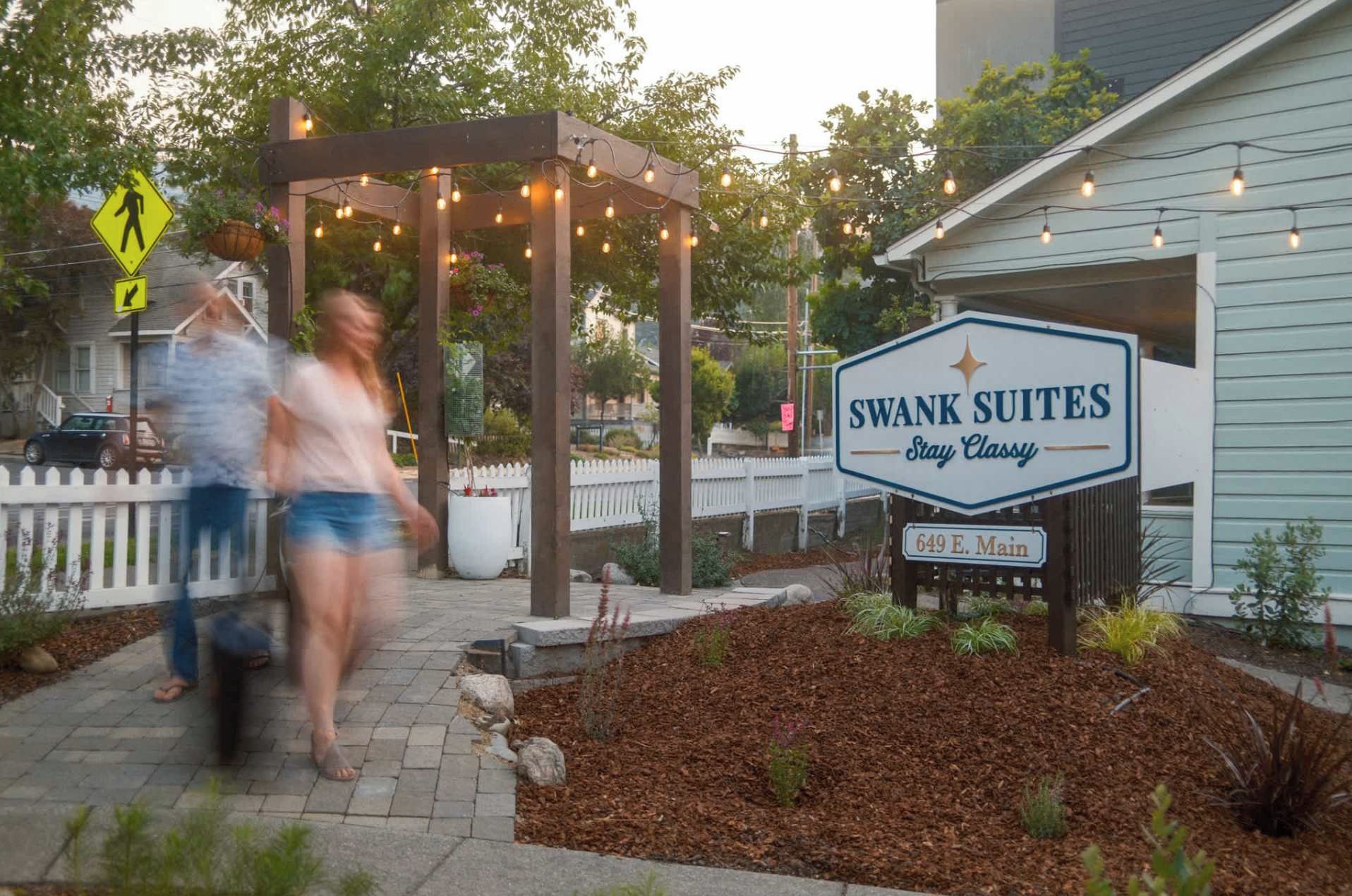 A hotel entrance with a sign for 'SWANK SUITES Stay Classy' and a pedestrian crossing sign.