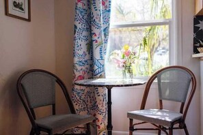 Una habitación con dos sillas, una mesita redonda y una ventana con cortinas.