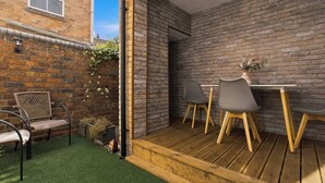Eine Terrasse mit Holzdeck, einer Ziegelwand und einem kleinen Tisch mit Stühlen.