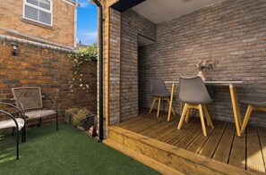 A patio with a wooden deck, a brick wall, and a small table with chairs. - WhiskAwayStays - Arboretum ground floor apartment (Worcestershire)