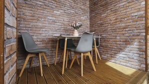 Ein Eckzimmer mit Backsteinwand, zwei graue Stühle, ein kleiner Tisch und eine Vase mit Blumen.