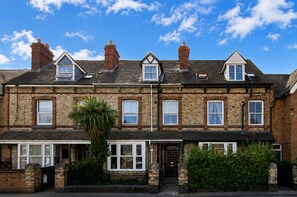 A two-story brick house with a front porch, multiple windows, and a chimney. - WhiskAwayStays - Arboretum ground floor apartment (Worcestershire)