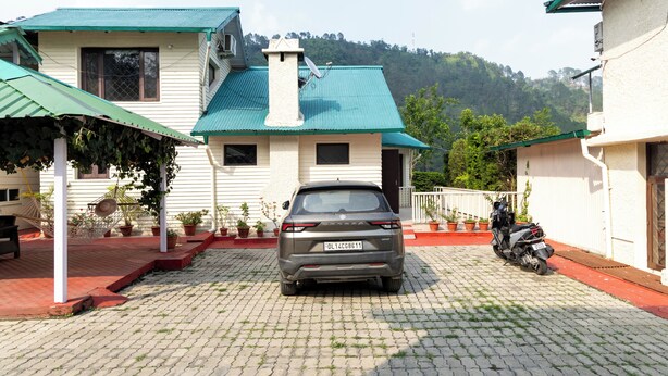 A residential area with a parked car and a motorcycle, paved driveway, and greenery. - Karinya Villas Scenic Hill View & Garden (Naina Range)