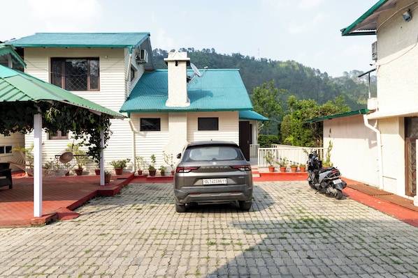 A residential area with a parked car and a motorcycle, paved driveway, and greenery.
