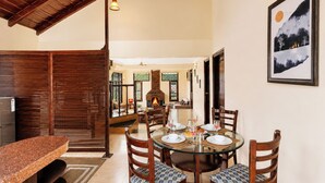 A dining area with a round glass table, wooden chairs, and a stone fireplace. - Karinya Villas Scenic Hill View & Garden (Naina Range)