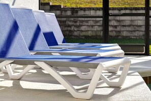 A row of lounge chairs with white frames and blue cushions, arranged on a concrete surface. - Private 4BR Retreat with Pool Near Disney (Championsgate)