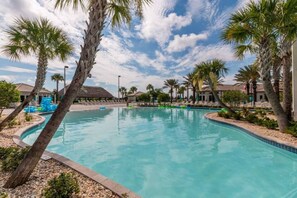 A swimming pool with palm trees, a clear sky, and a building in the background. - Private 4BR Retreat with Pool Near Disney (Championsgate)