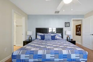 A bedroom with a large bed, two bedside tables, a ceiling fan, and a wall with a framed picture. - Private 4BR Retreat with Pool Near Disney (Championsgate)
