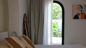 Um quarto com uma cama, um quadro, uma janela com cortinas e vista para o verde lá fora.