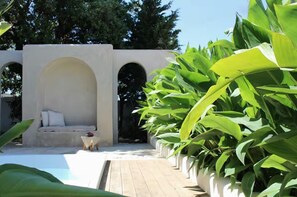 Un espace piscine doté d’un coin salon, le tout entouré d’une végétation luxuriante.