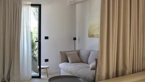 Uma sala de estar moderna com um sofá, uma mesa de centro redonda e uma porta de vidro deslizante que dá para uma varanda.