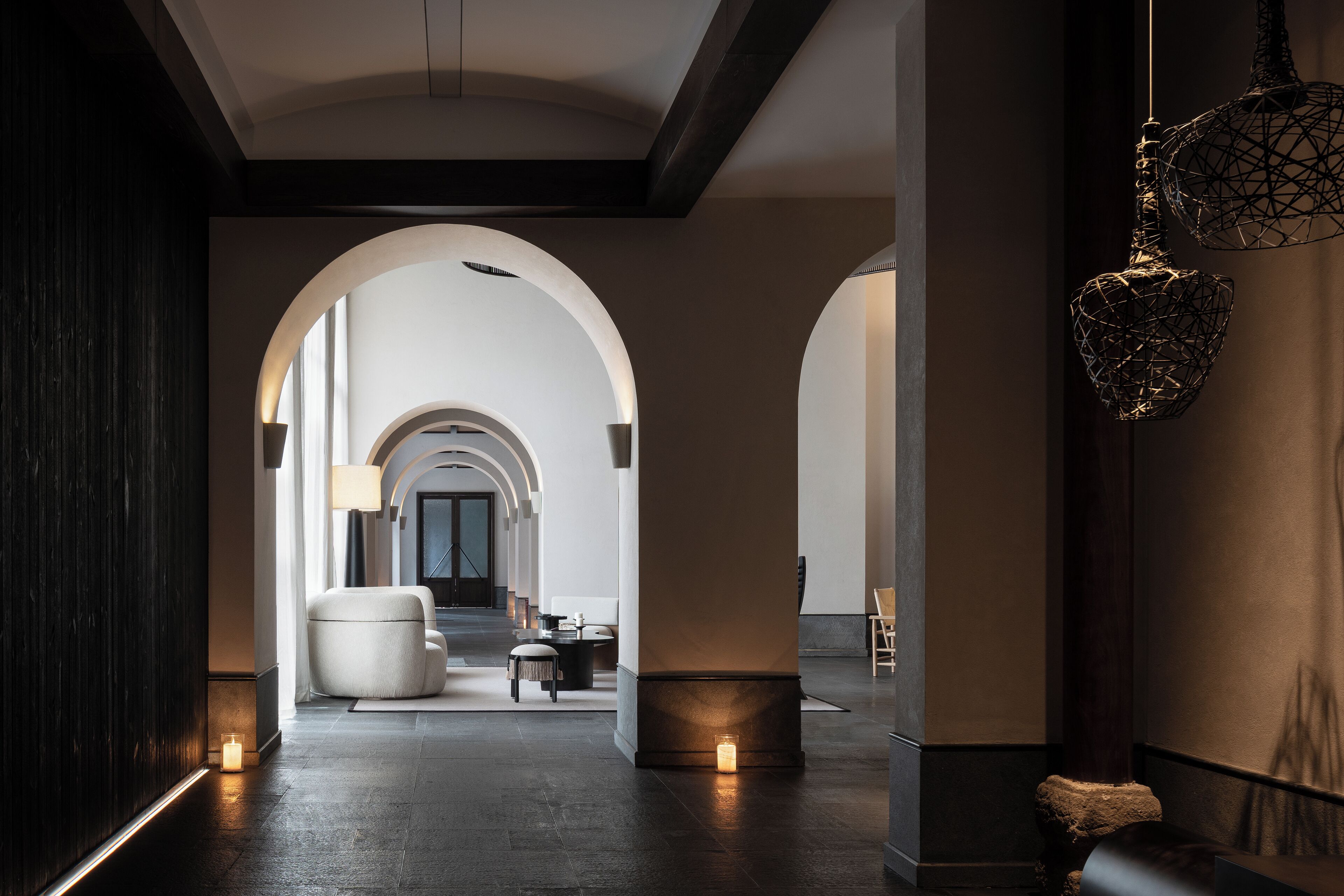 A modern interior with a central arched corridor leading to a seating area, featuring a minimalist design with a dark floor and neutral walls.