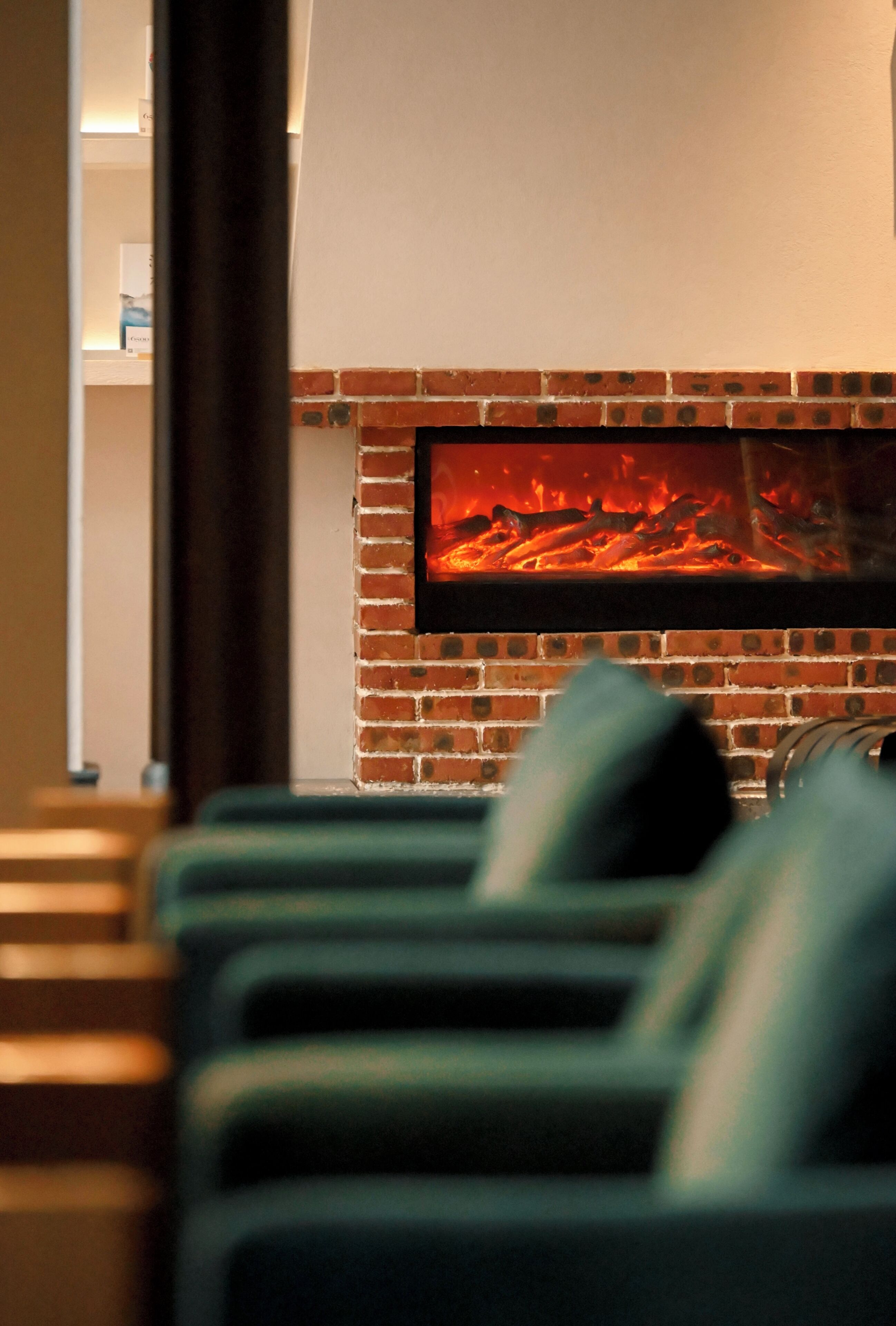 A room with a brick fireplace, a television mounted above it, and green upholstered seating.