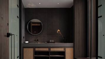 Un baño moderno con una pared de azulejos oscuros, un espejo redondo, un lavabo con encimera oscura y una mopa en el suelo.