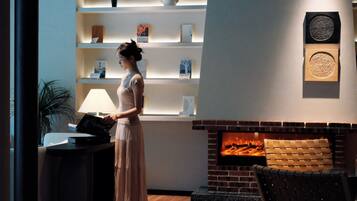 A woman in a room with a fireplace, a bookshelf, and a lamp.