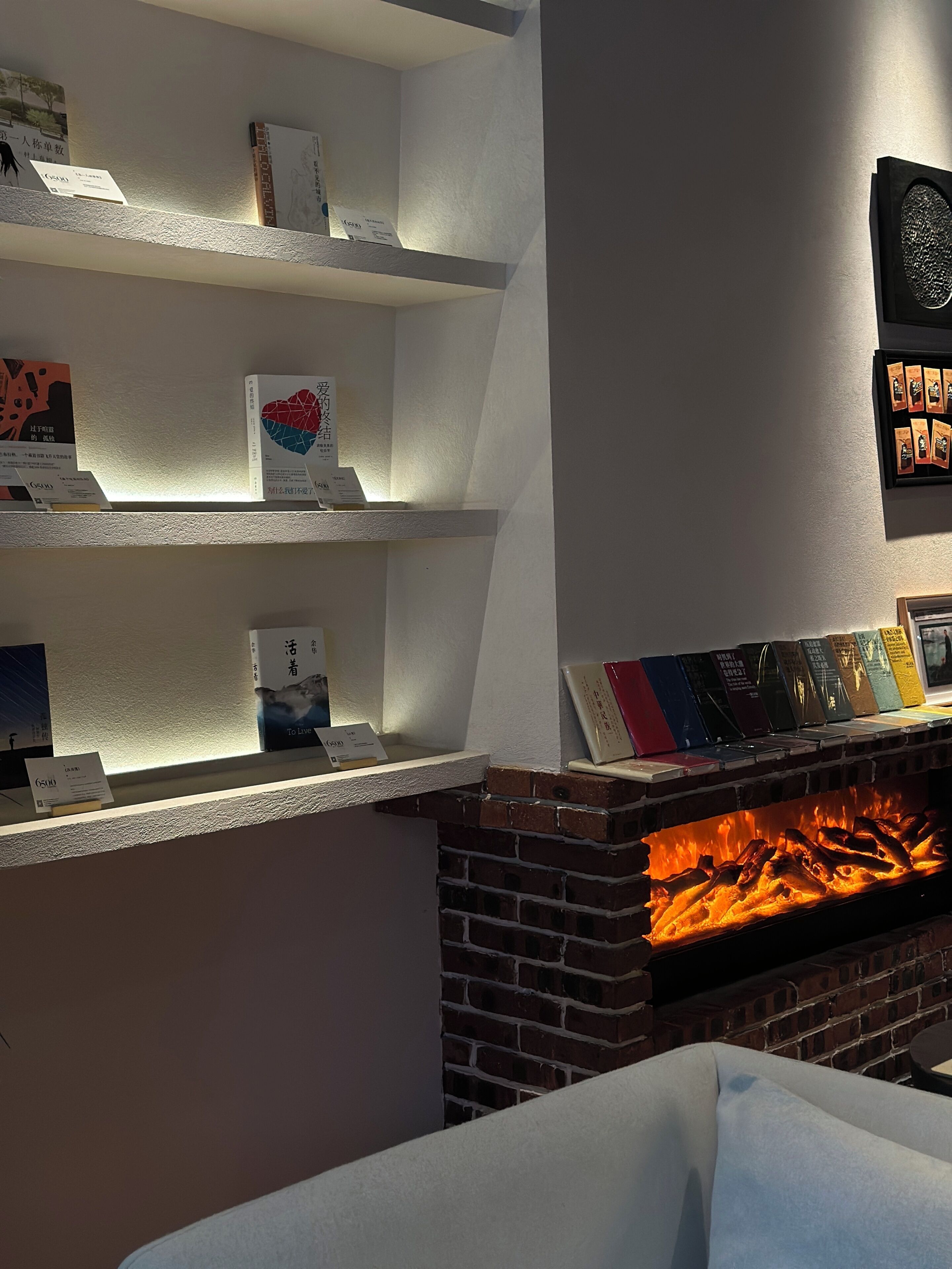 Una habitación con chimenea de ladrillo, estanterías blancas con libros y juegos, y un cuadro en la pared.