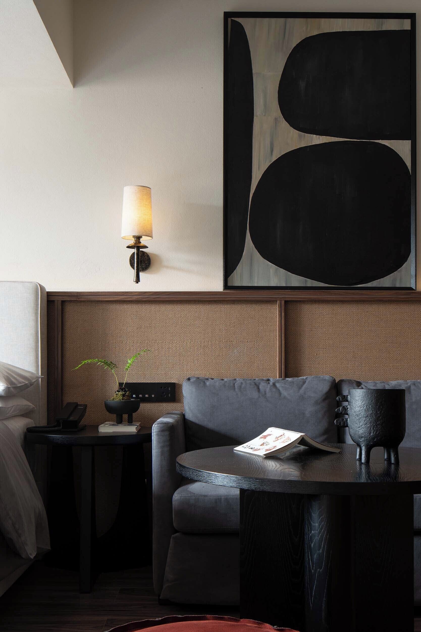 Habitación de hotel moderna con un cuadro abstracto grande, una lámpara de pared, un sofá, una mesita auxiliar con una planta y una mesa de centro.