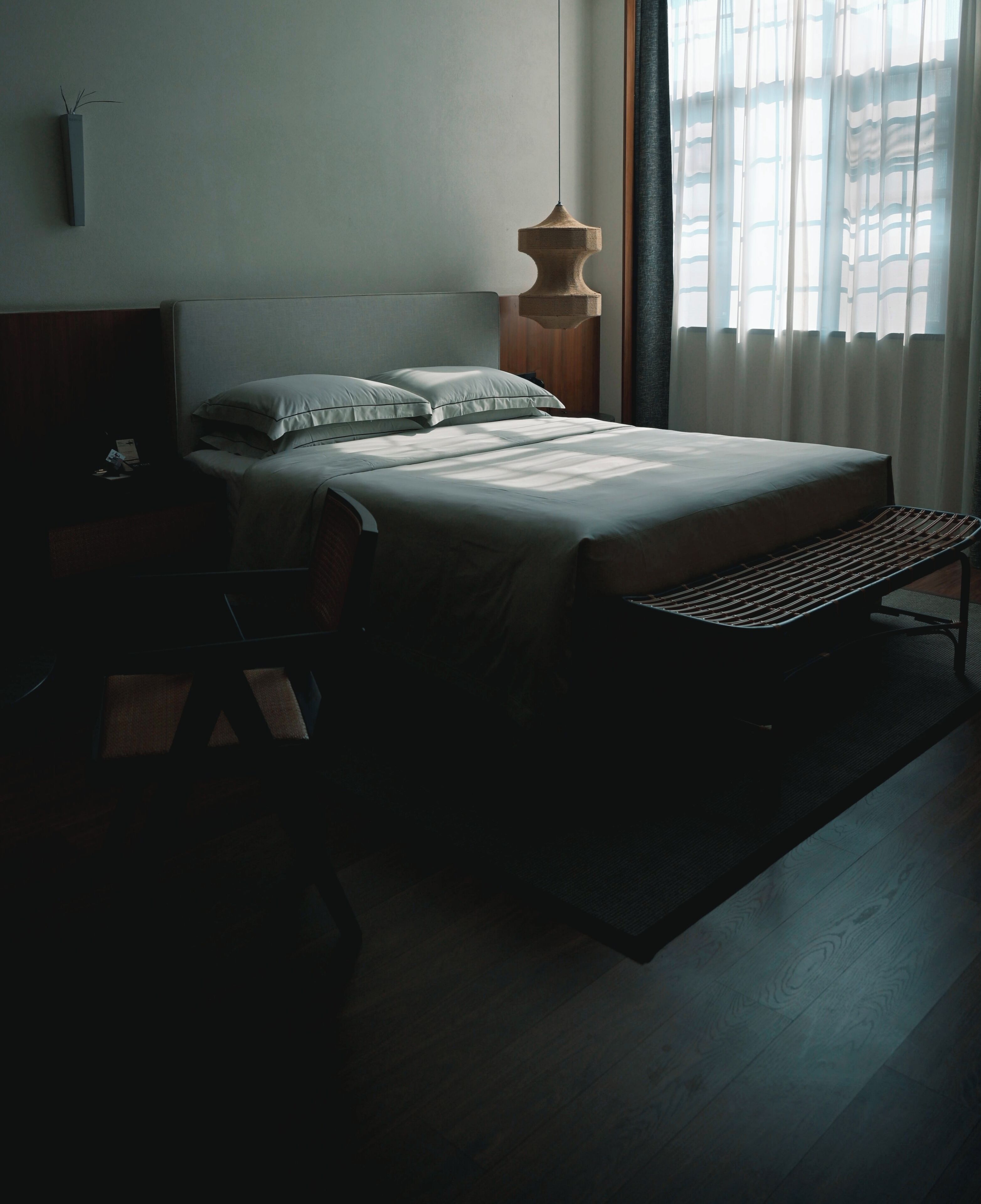 A bedroom with a bed, a bench, a desk, and a window with curtains.