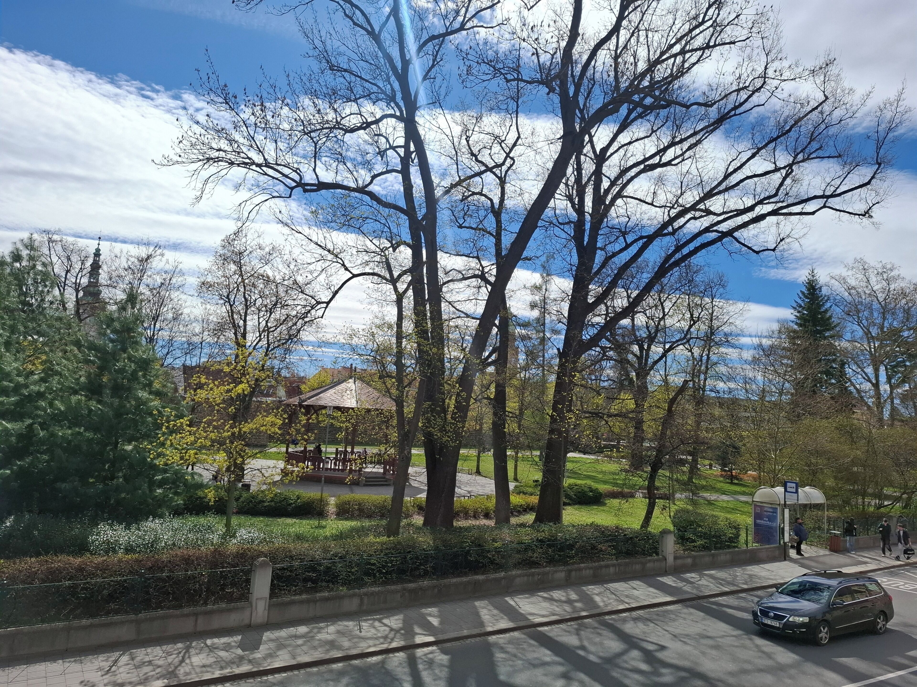 A park with a gazebo, trees, and a distant building.