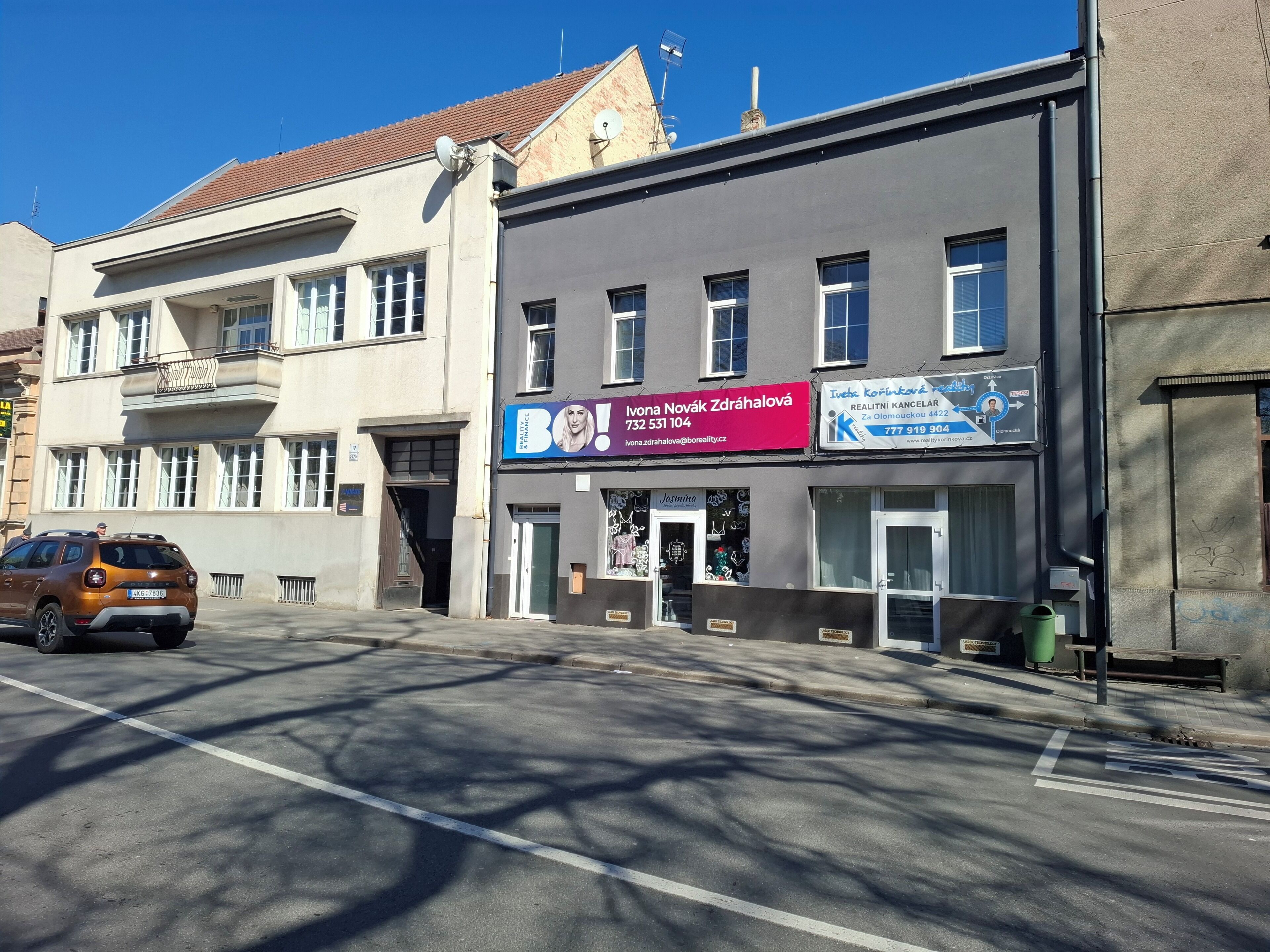 En gatubild med en byggnad som har en röd skylt för en skönhetssalong och en blå skylt för en fastighetsbyrå.