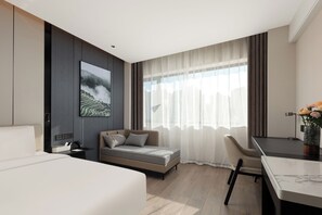 Habitación de hotel moderna con cama, escritorio, silla y un amplio ventanal con cortinas.