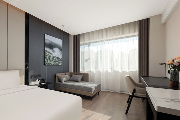 A modern hotel room with a bed, a desk, a chair, and a large window with curtains.