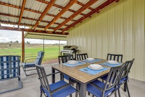 Un espace extérieur aménagé pour les repas, avec une table et des chaises en bois, un barbecue et une vue sur la campagne.
