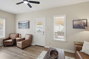 A living room with a ceiling fan, two leather chairs, a coffee table, and two windows with blinds.