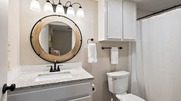 A bathroom with a round mirror, a sink, a toilet, and a shower curtain.