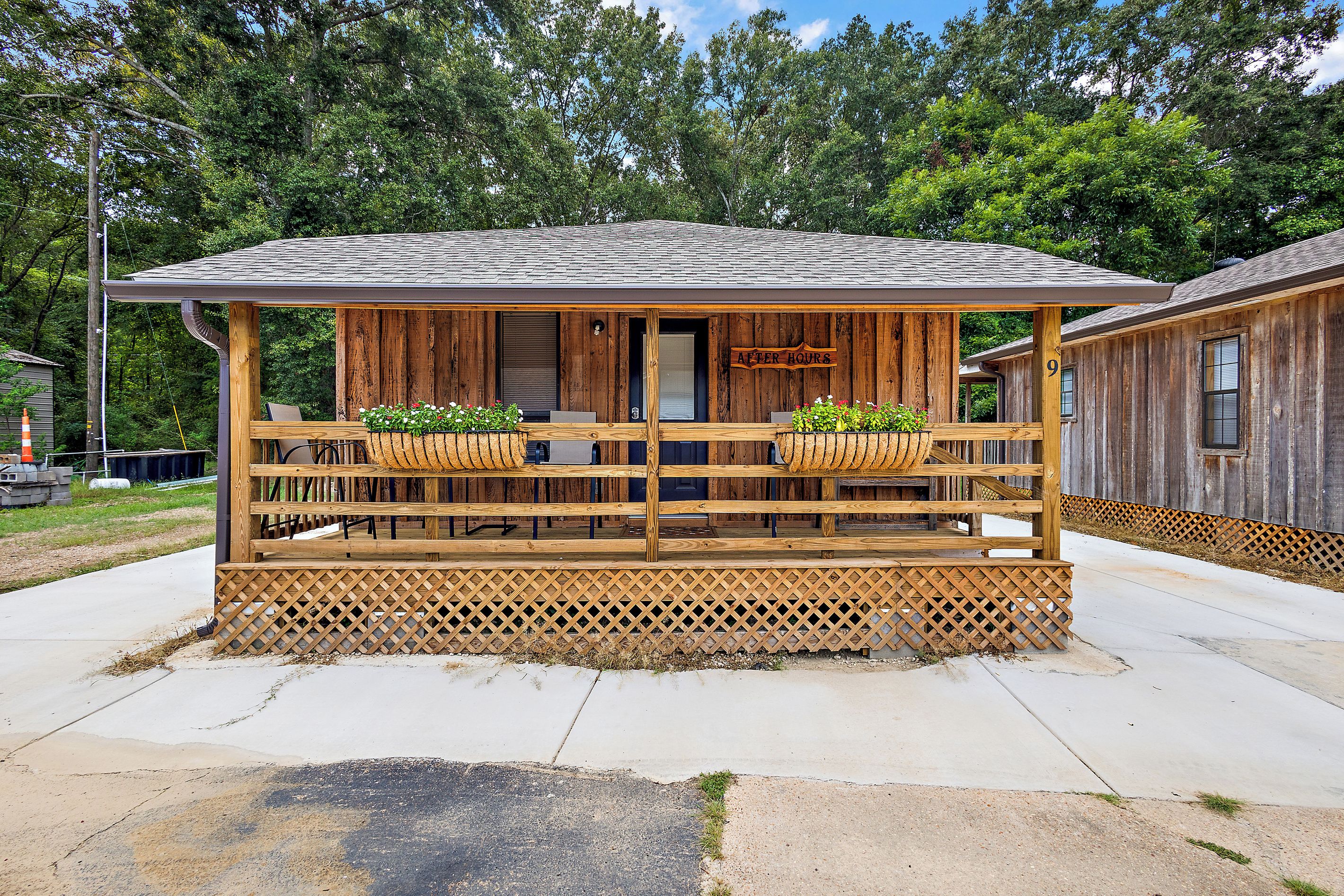 A wooden cabin with a porch, a sign reading 'AFTER HOURS', and two flower baskets.