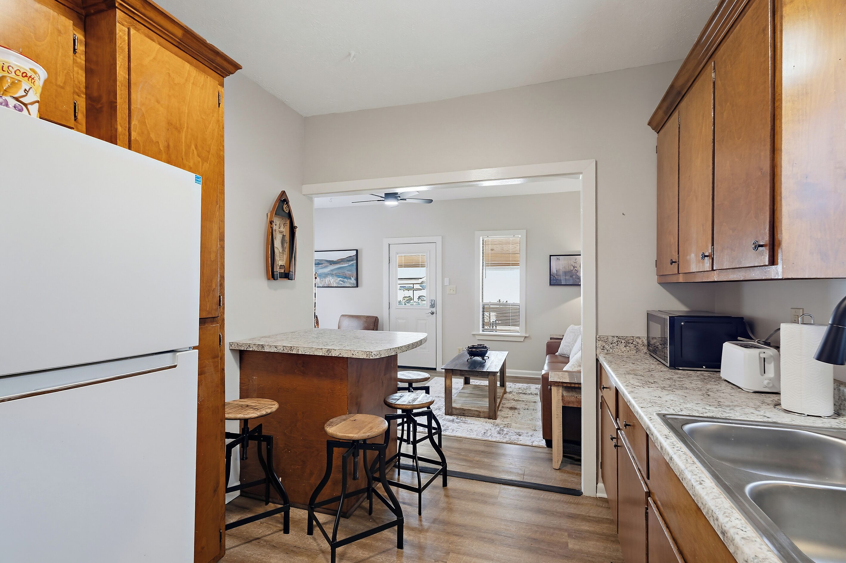 A kitchen with wooden cabinets, a white refrigerator, a granite countertop, and a dining area with a table and chairs.