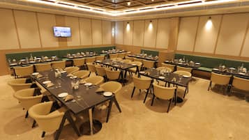 Une salle de conférence équipée de plusieurs tables et chaises, d’un téléviseur à écran plat fixé au mur et d’un banc vert rembourré le long du mur.