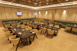 A conference room with multiple tables and chairs, a flat-screen TV mounted on the wall, and a green cushioned bench along the wall. - Ananta Elite (Somnath)