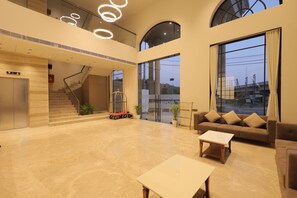 A spacious lobby with a marble floor, a sofa, a coffee table, and a staircase leading to an upper level. - Ananta Elite (Somnath)