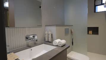 Un baño moderno con un espejo grande, un lavamanos, un inodoro y una zona de ducha.