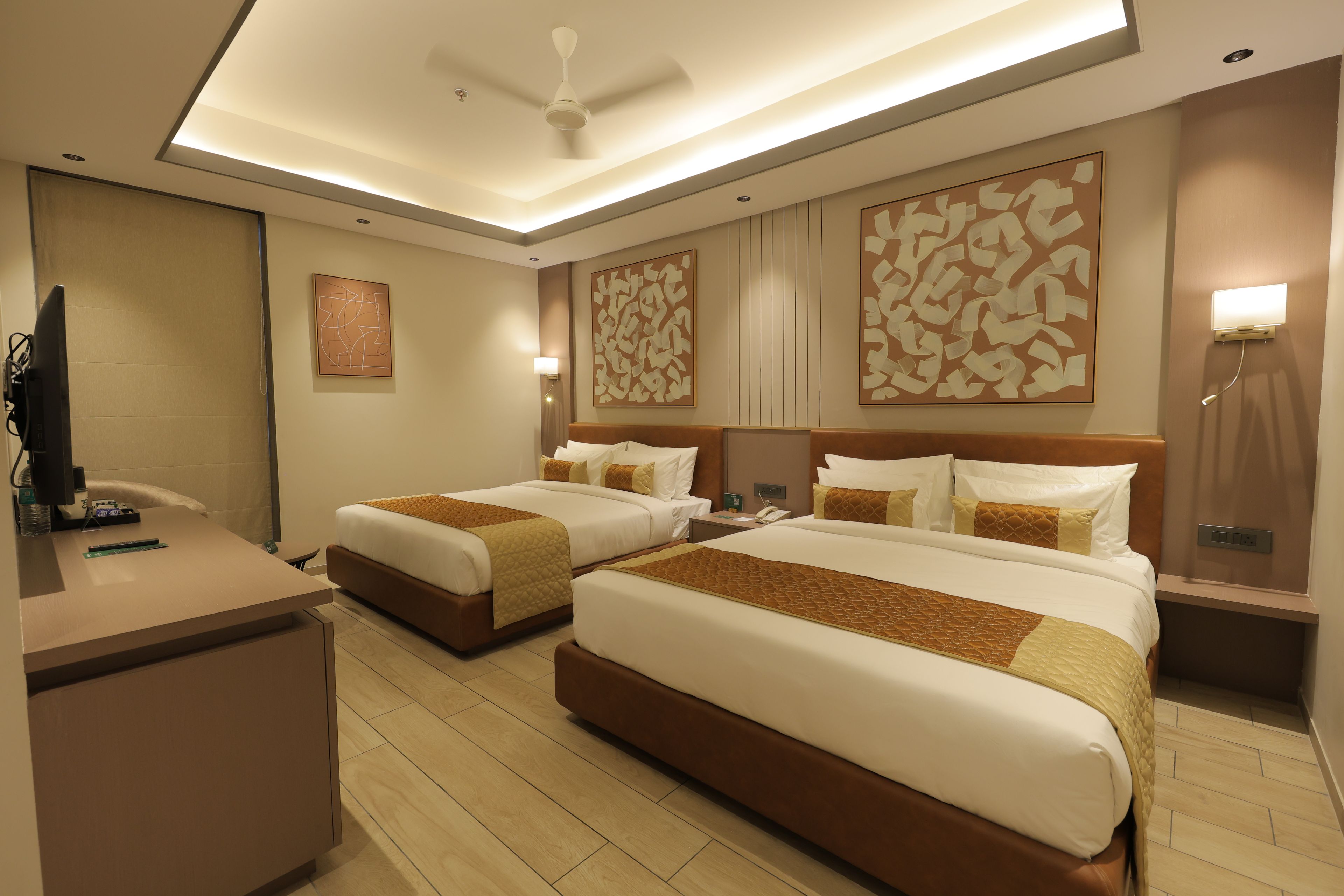 A hotel room with two beds, a desk, a flat-screen TV, and artwork on the walls.