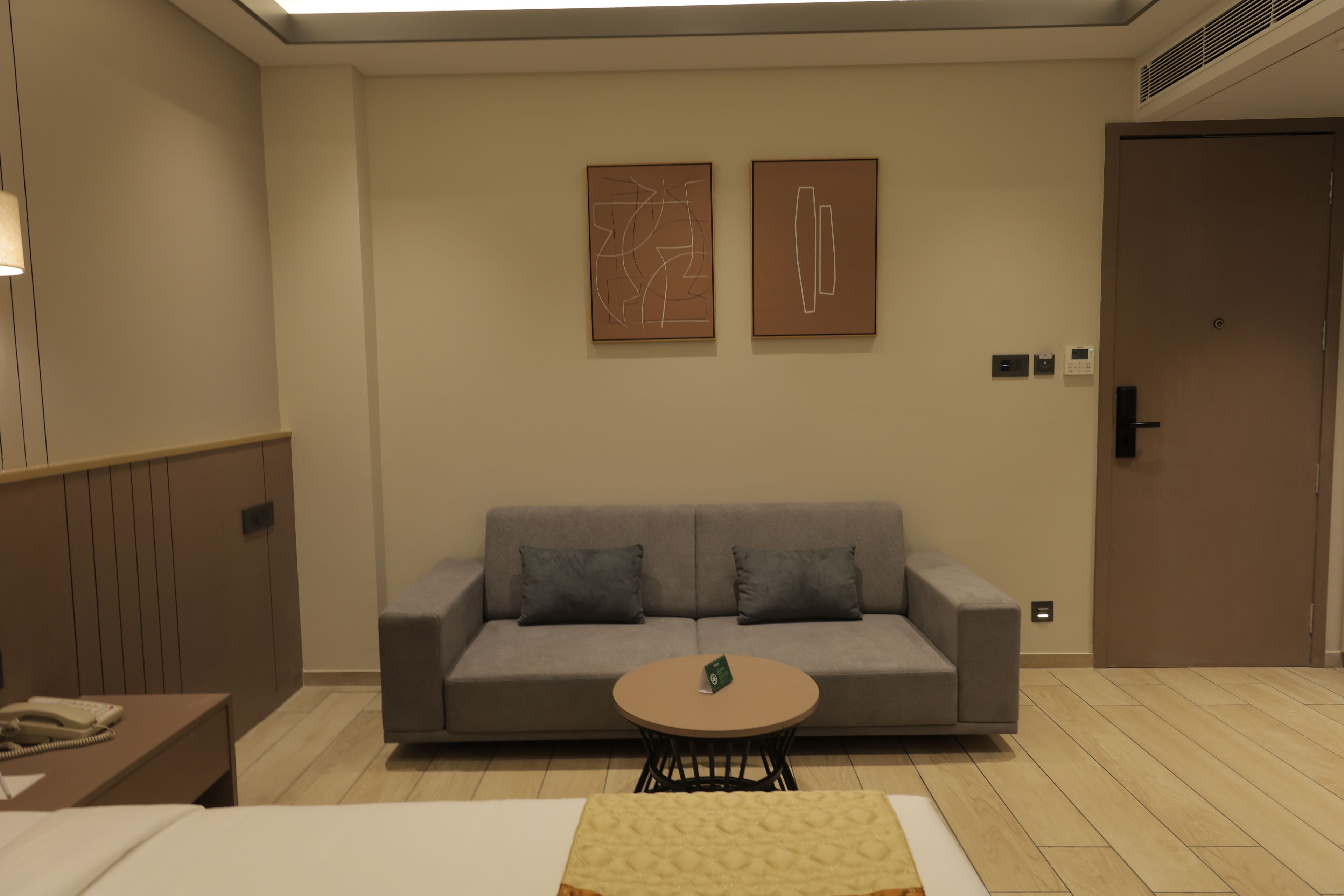 A hotel room with a grey sofa, a small round table, and two abstract paintings on the wall.